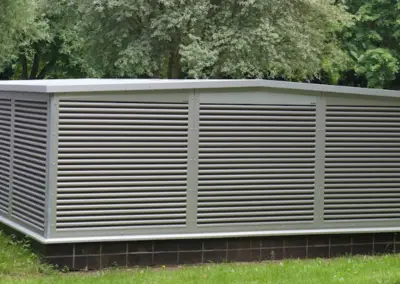 Klimaeinhausung von rotec mit horizontalen Lamellen zur Abschirmung von technischen Außengeräten in einer Grünanlage