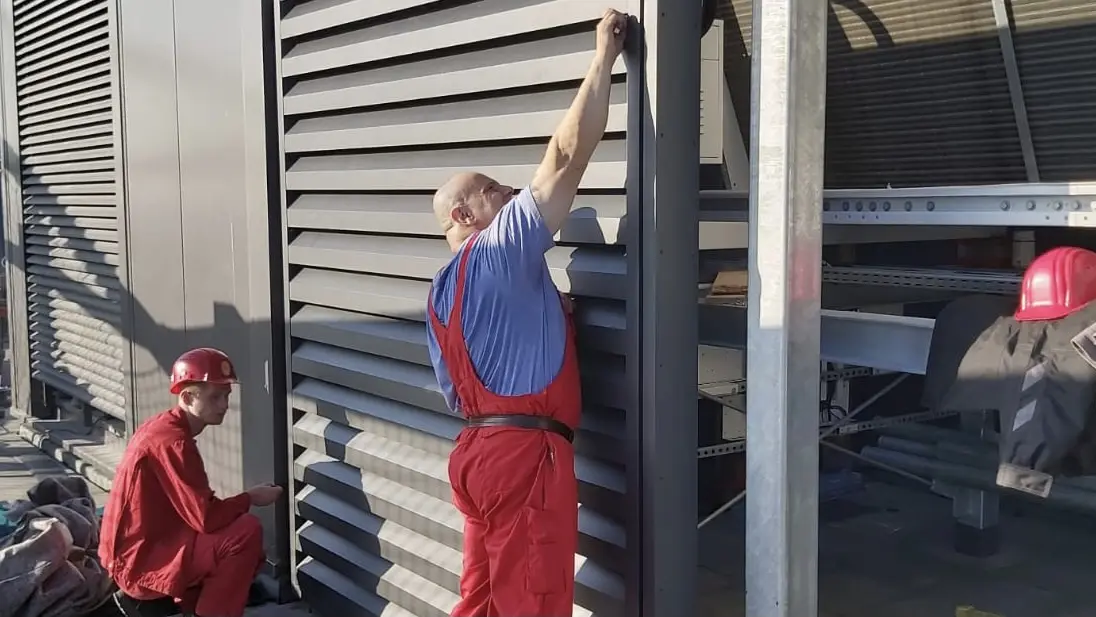 Zwei rotec Monteure montieren horizontale Aluminiumlamellen an einer technischen Dachanlage.